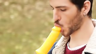 Handsome man is sitting on the bench where he is sucking on a lollipop that is shaped like a dick
