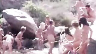 Pretty couple of girls wearing bathing suits get naked in a river alongside many dudes with a vintage vibe