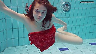 Red haired girl Libuse swimming in a pool in fire red dress