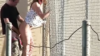 Dear in a polka dot black and white dress hangs onto a fence while she is fucked outdoors.